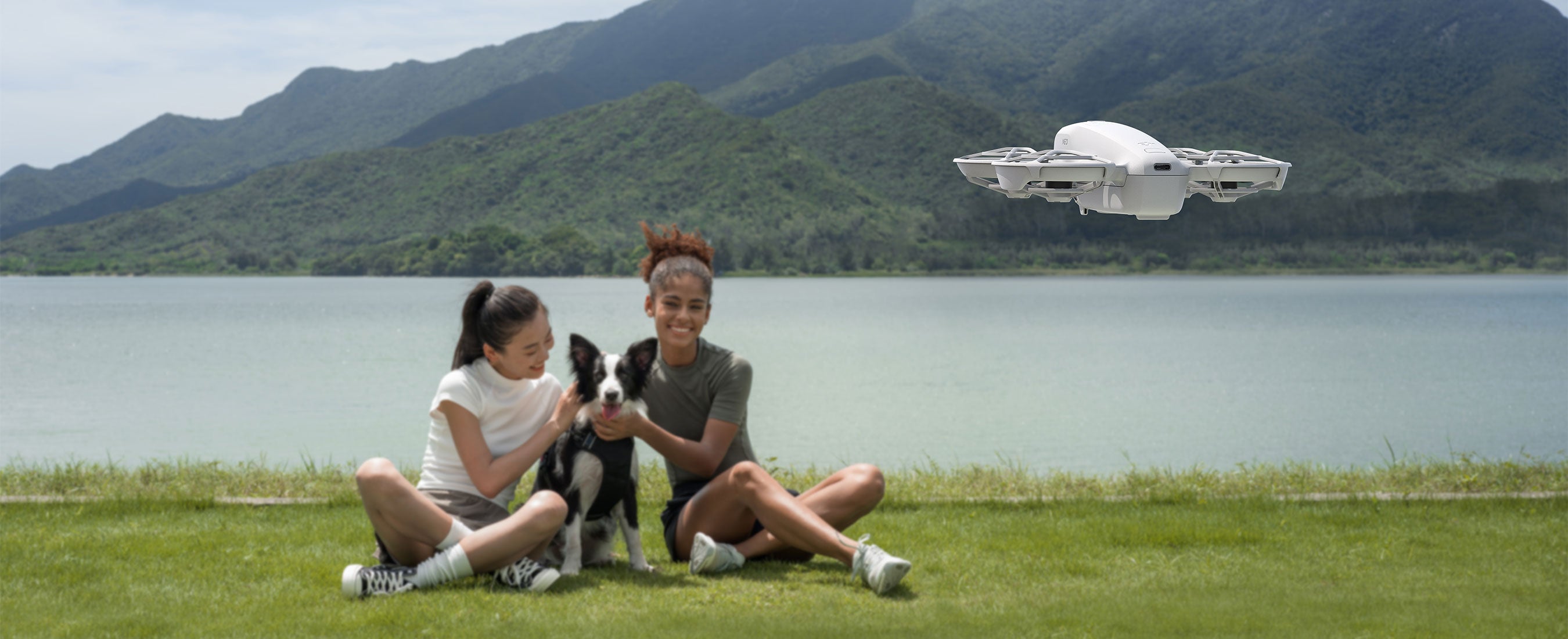 DJI Neo taking a picture of two girls with their dog in front of a landscape.