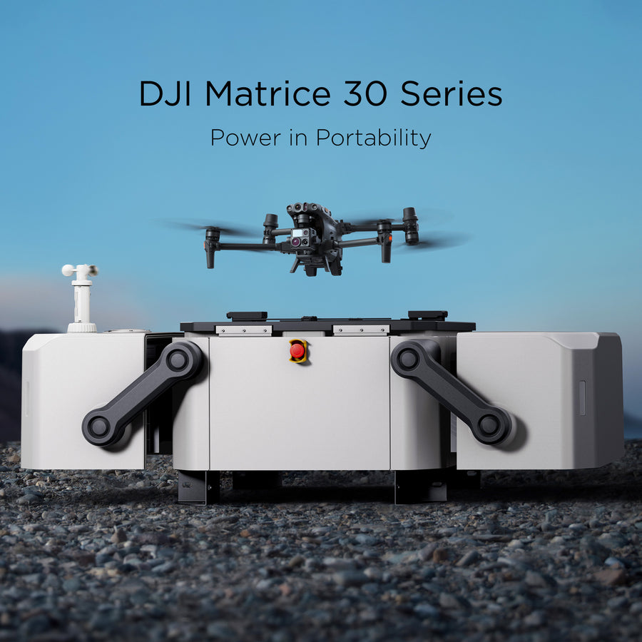 A DJI Matrice 30 series hovers above a DJI Dock resting upon rocky terrain during a sunny day.