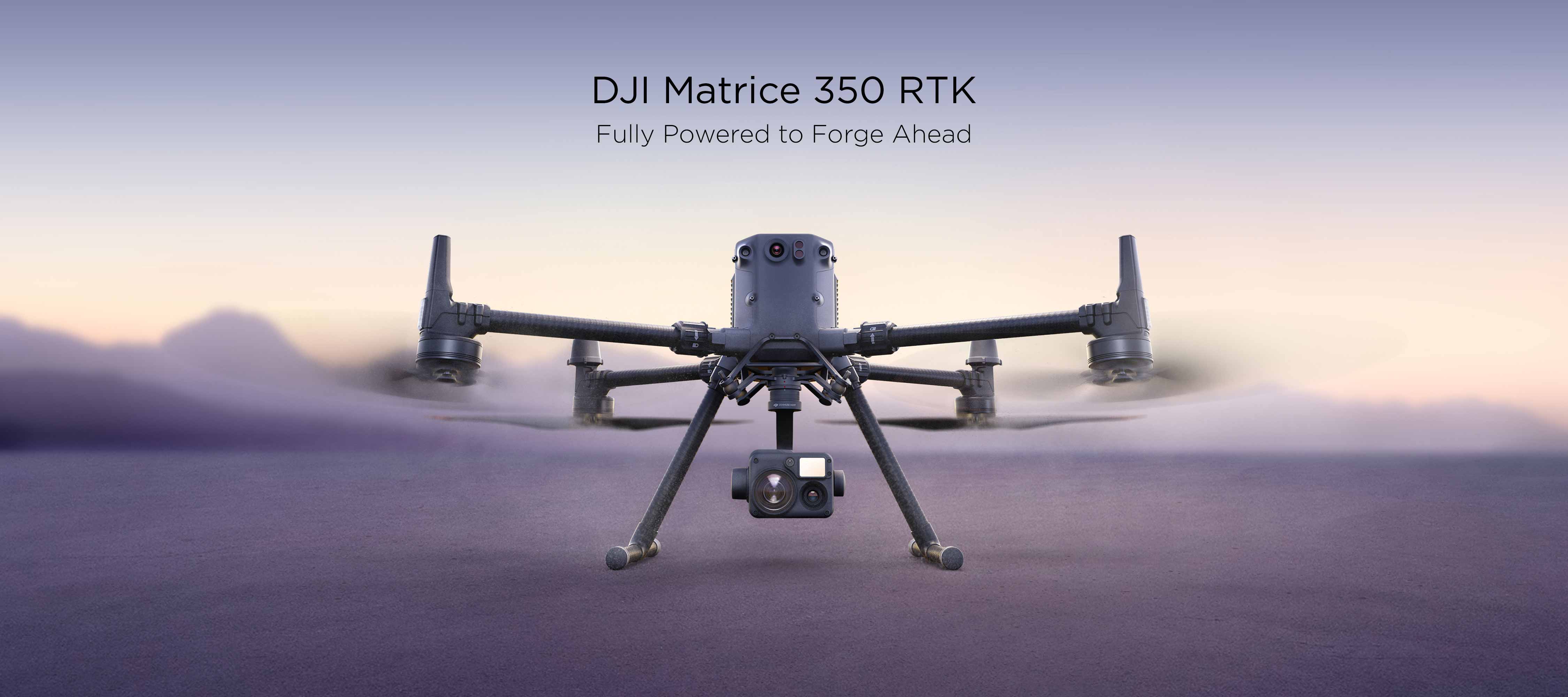 The DJI Matrice 350 RKT landed on sandy terrain with the propellers spinning, a DJI Zenmuse H20T is mounted to the drone.