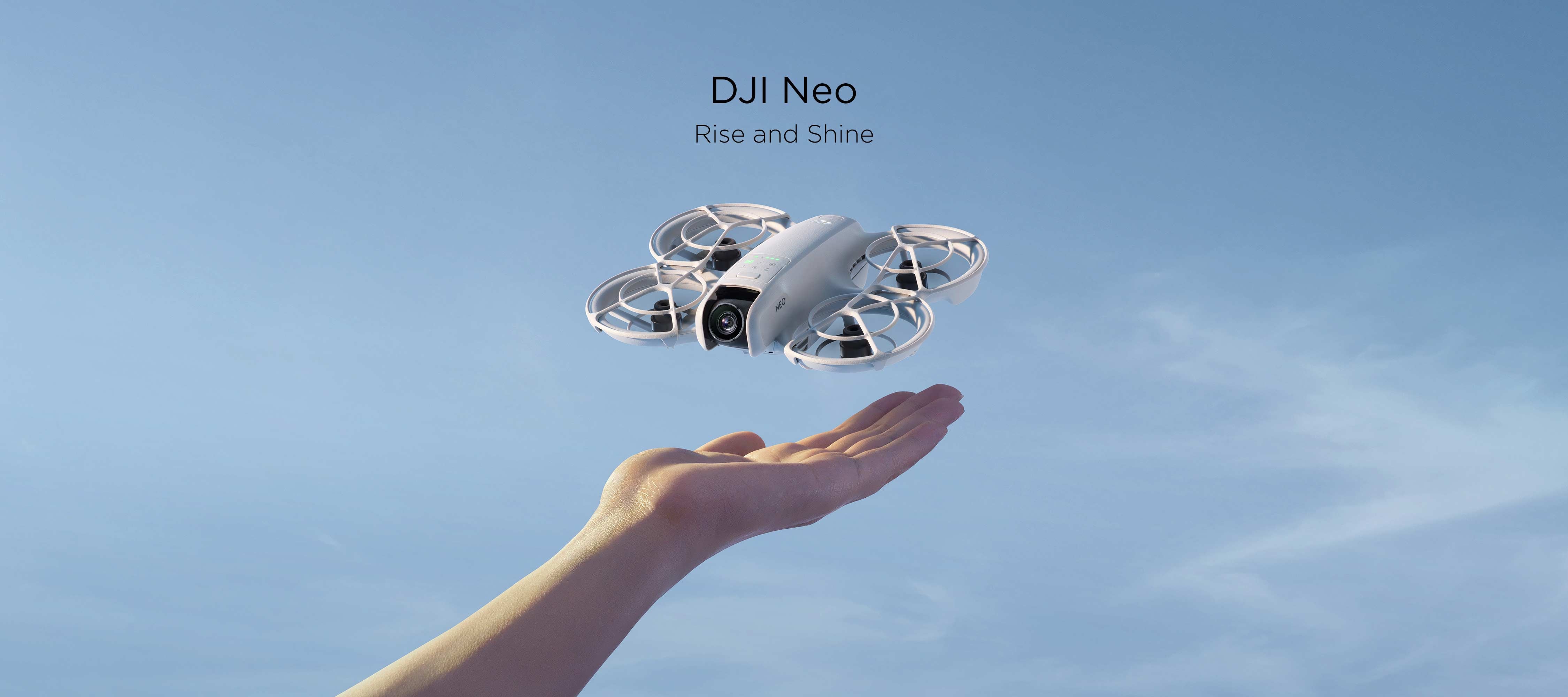 A DJI Neo hovering above a person's outstretched hand against a blue sky.